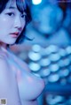 A naked asian woman posing in front of a blue light.