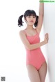 A woman in a pink bathing suit leaning against a wall.