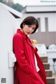 A woman in a red coat leaning against a wall.