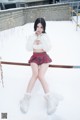 A woman in a white sweater and red plaid skirt posing in the snow.