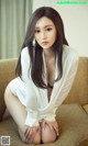 A woman sitting on top of a couch in a white shirt.