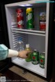 A person is opening a small refrigerator with drinks in it.