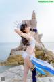 A woman in a bikini standing on a rock by the ocean.