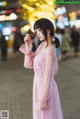 A woman in a pink dress standing on a city street.