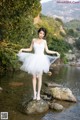 A woman in a white dress standing on a rock in the water.