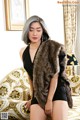 A woman in a black dress and fur vest posing on a couch.