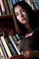 A woman sitting in front of a bookshelf holding a book.