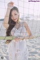 A woman in a white dress holding a surfboard on the beach.