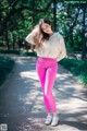 A woman in bright pink leggings and a beige hoodie poses for a picture.