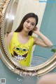 A woman in a yellow tank top is looking at herself in a mirror.