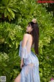 A woman in a blue dress standing in front of a bush.