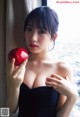 A woman in a black dress holding an apple.