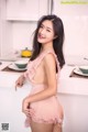 A woman in a pink lingerie posing in a kitchen.